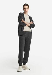Kulgrå strikket cardigan over en cremefarvet sweater, parret med matchende bukser. Struktureret stof, ribbede manchetter og letvægtige sneakers.