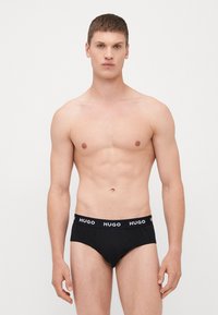 Schwarze Herrenunterwäsche mit einem weichen Bund, der das Logo "HUGO" in Weiß trägt. Das Design ist glatt, figurbetont und minimalistisch ohne zusätzliche Muster.