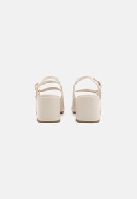 Sandales à talons bloc beige avec trois straps ajustables. Matériau lisse avec un design de talon rectangulaire et un détail de boucle minimaliste.
