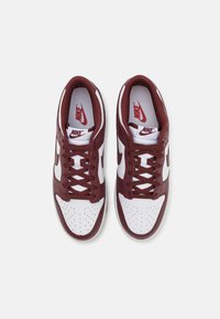 Nike sneakers with a burgundy leather upper and white accents. Features include perforated toe box, laces, and tongue logo.