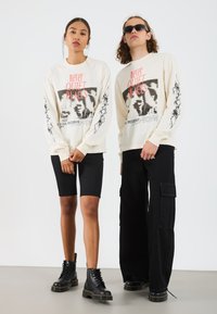 Long-sleeve cream graphic tees feature black and red print; paired with black shorts and pants. Black lace-up boots complete the look.
