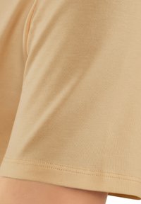 Bawełniana koszulka w jasnym beżu, z gładką fakturą, krótkimi rękawami oraz starannym przeszyciem u dołu.