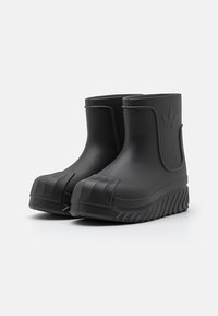 Botas de goma negras hasta el tobillo con una suela texturizada y puntera moldeada. Presentan un logo elevado en el lateral y un material suave e impermeable.