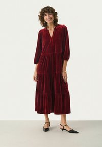 Röd sammet maxi-klänning med ett lagerdesign, långa ärmar och en nyckelhals. Matchad med svarta slingback-skor.