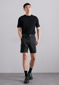 Musthave musta lühikeste varrukatega t-särk, kohandatud mustad lühikesed püksid, must vöö hõbedase pandlaga, mustad sokid ja sujuvad mustad kingad. Ühtne sile pind kogu riietuses.