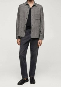 Camisa de patrón a cuadros en blanco y negro, de corte relajado, con frontales abotonados y un solo bolsillo en el pecho; combinada con jeans rectos de pierna negra y zapatos negros.