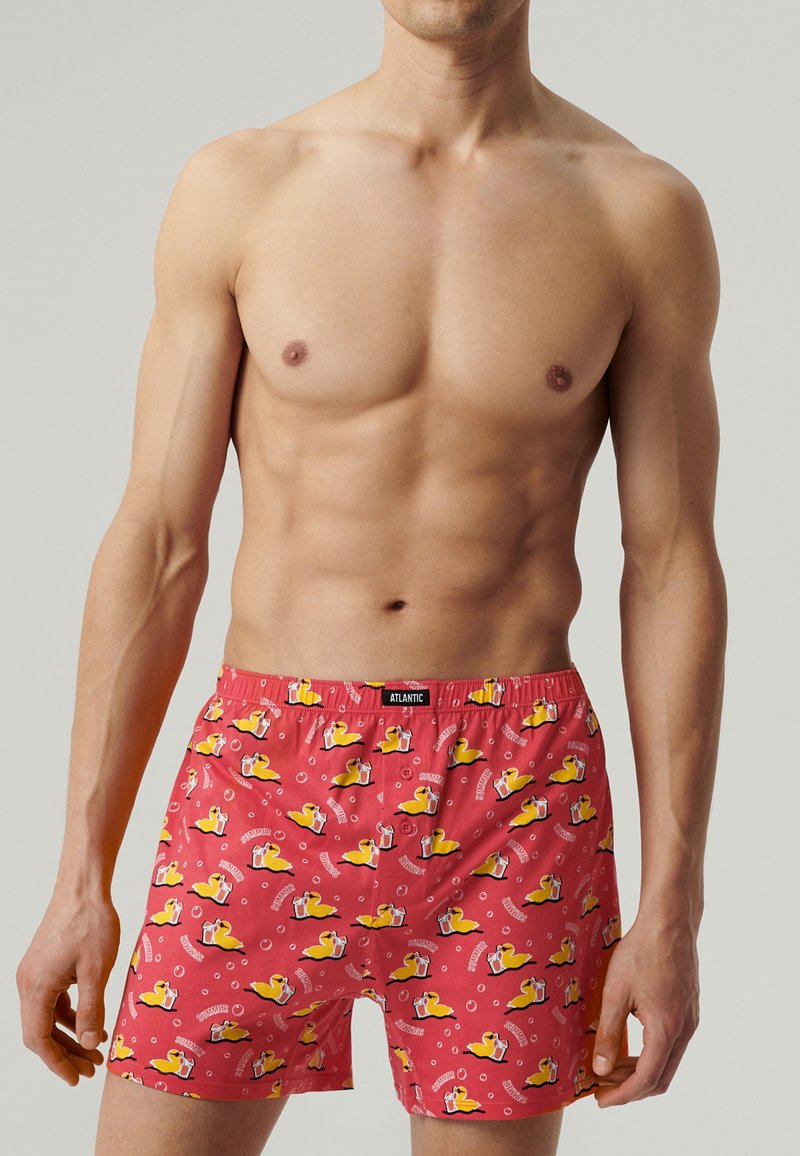 Czerwone bokserki z wzorem gumowych kaczek i bąbelków, wykonane z lekkiego materiału, z elastycznym pasem ze znakiem towarowym.