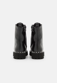 Bottines en cuir verni noir avec une semelle épaisse et texturée, ornées de perles autour de la base. Fermeture éclair à l'arrière.