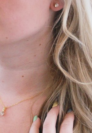 Goldene Kettenhalskette mit einem klaren, runden Anhänger. Kleine Steckerohrringe und mehrfarbige Nägel in den Farbtönen Grün, Blau und Gelb.