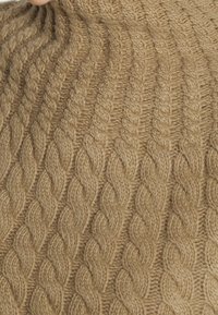 Pull en tricot en fil beige doux avec un motif en torsades. La texture est épaisse et côtelée, offrant une apparence confortable et chaude.