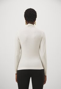 Langärmliges, tailliertes Turtleneck-Top aus leicht beigem Rippstoff mit hohem Kragen und nahtlosen Schultern, kombiniert mit schwarzen Leggings.