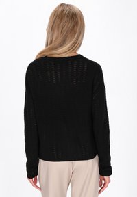 Zwarte, gebreide trui met een losse pasvorm, voorzien van een chevronpatroon, lange mouwen en een ronde hals, gezien van achteren.