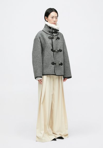 Sivi vuneni kaput s visokim ovratnikom, zatvaranjem na preklop i bijelim ovsenim podstavom. Uparen s širokim, kremastim hlačama.