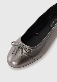 Metallic grey ballet flat with a rounded toe, a textured finish, and a small bow accent on the vamp. Black interior and minimalistic design.