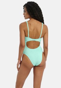 Maillot de bain une pièce vert menthe avec un tissu texturé, des bretelles réglables et une grande découpe dans le dos. Détail de fermeture à crochets.