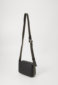 Rectangular sling bag with a textured black leather exterior, green fabric strap, and silver hardware. Simple, functional design.