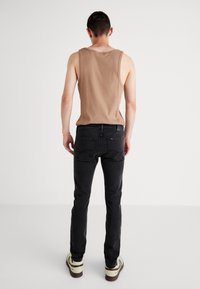 Smešana majica bez rukava u boji tan, crne tanke jeans hlače i svijetle tenisice. Tkanina je glatka, s opuštenim krojem i minimalnim detaljima.