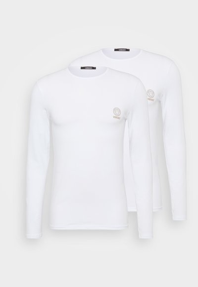 Ilgų rankovių balti marškiniai, pagaminti iš medvilnės, su apvalia kaklo iškirpte, su mažuoju auksiniu liūto logotipu ant kairiojo krūtinės kampo. Du identiški marškiniai.