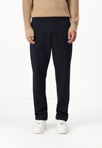 Marinblå rutiga byxor med elastisk midja och avslappnad passform. Tillverkade av ett mjukt tyg, kombinerat med vita sneakers.