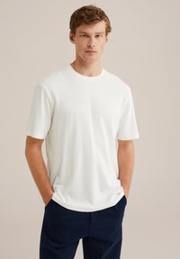 Camiseta blanca de textura con mangas cortas y escote redondo, combinada con pantalones azul marino. Diseño sencillo, tejido ligero, ajuste casual.