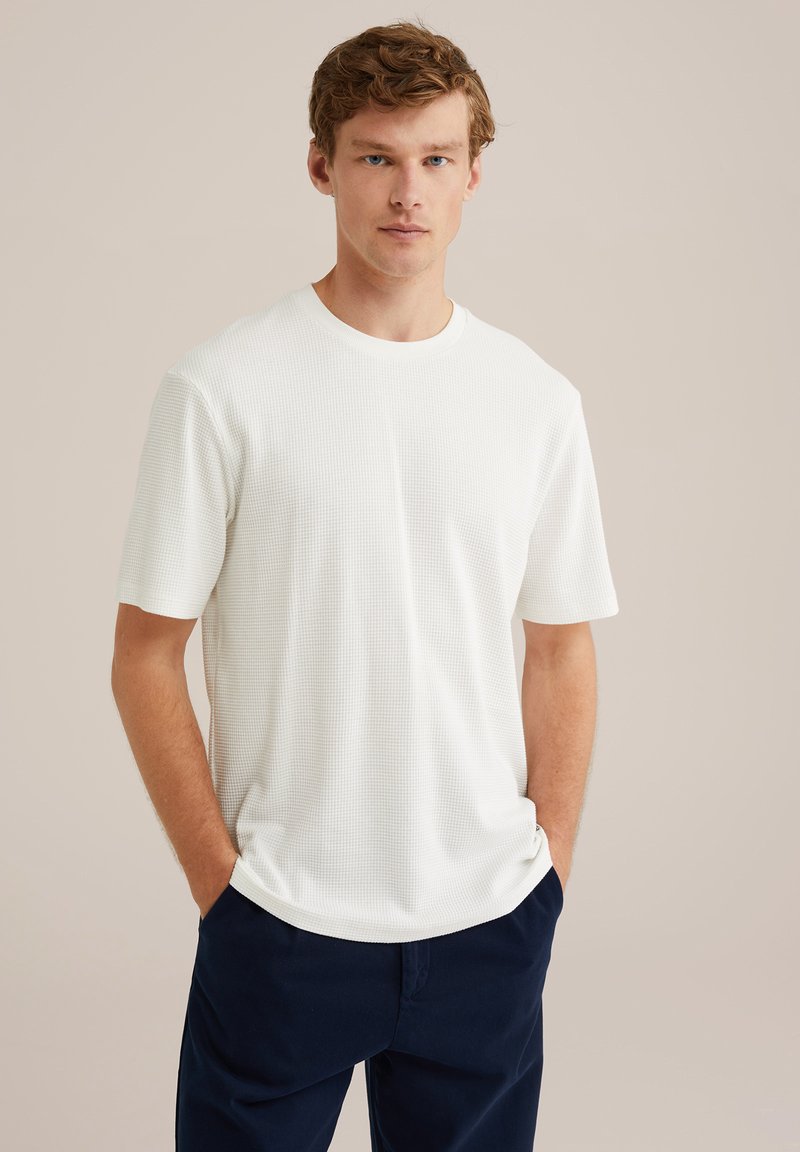 Camiseta blanca de textura con mangas cortas y escote redondo, combinada con pantalones azul marino. Diseño sencillo, tejido ligero, ajuste casual.
