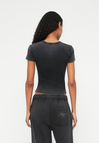 Zwarte aansluitende t-shirt met korte mouwen en een ronde hals, met een vervaagde textuur. Gecombineerd met losse grijze sweatpants met geborduurde details op de zak.