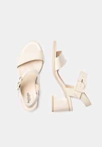 Sandales en cuir verni beige avec deux larges brides, une boucle latérale et un talon bas et épais. Texture lisse avec un design minimaliste.