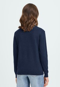 Mørkeblå sweater med rund halsudskæring, lange ærmer og ribstrikkede manchetter og kant, lavet af blødt strikkemateriale. Bagsiden viser et minimalistisk design.