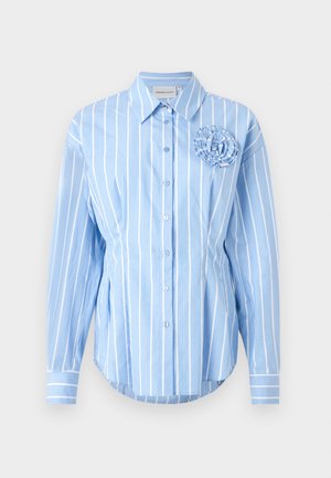 Camisa azul clara de botones con rayas verticales blancas, que presenta un detalle de flor de tela en el lado izquierdo del pecho y puños ajustados.