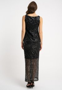 Czarna, bezrękawnikowa sukienka cekinowa z dopasowaną sylwetką; przezroczysta dolna połowa odsłaniająca nogi; teksturowana błyszczącymi cekinami; widok od tyłu.