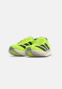 Zapatillas de correr verde neón con acentos negros, diseñadas con una forma aerodinámica, parte superior texturizada y detalles grises en la lengüeta y la suela.