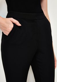 Svarta skräddarsydda byxor med en mjuk yta, som har en midje med normal höjd och sidofickor. Minimalistisk design utan synliga mönster.