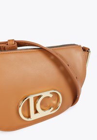 Borsa a tracolla in pelle marrone con un design elegante, caratterizzata da un logo dorato e una chiusura con zip, posata su uno sfondo bianco.