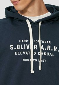 Felpa navy con cappuccio e coulisse, con testo bianco: "S. OLIVER A.R.R. ELEVATED CASUAL BUILT TO LAST." Tessuto misto cotone con una consistenza morbida.