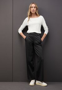 Blusa blanca de manga larga con escote barco, combinada con pantalones de pierna ancha gris oscuro con detalles de botones y bolsillos laterales. Zapatillas blancas.