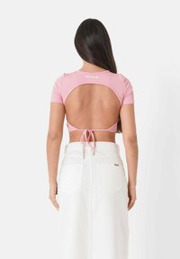 Top corto a coste rosa con maniche corte e schiena aperta, dotato di chiusura a fiocco. Abbinato a una gonna lunga in denim bianca con tasche posteriori.
