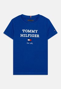 Modré bavlněné tričko s bílým logem "TOMMY HILFIGER", pod kterým se nachází malé vlajkové logo a text "Est. 1985". Krátké rukávy a kulatý výstřih.