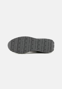 Semelle de chaussure en caoutchouc gris avec une surface à motifs mettant en avant le logo "TOMMY JEANS" répété, de forme arrondie et avec une finition texturée.