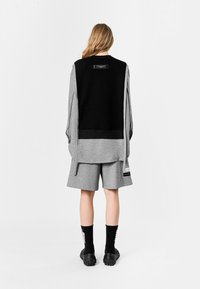 Pantalones cortos grises y una sudadera de capas en negro y gris con una etiqueta negra en la parte posterior. Cuenta con mangas largas y detalles de cordón.