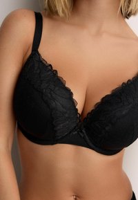 Reggiseno nero con bordatura in pizzo, tessuto a pois, spalline regolabili e forma a triangolo con finitura liscia e dettagli di texture sottili.