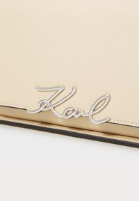 Borsa in pelle beige con logo firmato in argento "Karl", con cuciture visibili e un accento nero lungo il bordo inferiore.