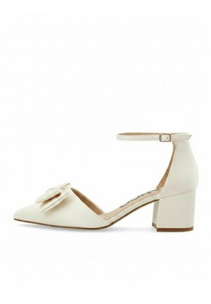 Kremowe damskie buty na niskim słupku, z ostrym noskiem, paskiem wokół kostki z klamrą oraz ozdobną kokardą z przodu.