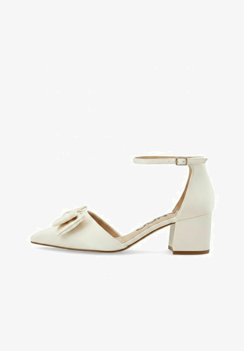 Chaussure pour femme à talon carré bas de couleur crème, avec bout pointu, bride à la cheville avec boucle, et nœud décoratif à l'avant.