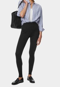 Czarne legginsy o wysokim stanie w połączeniu z białym podkoszulkiem i niebiesko-białą koszulą w paski z guzikami. Wpleciona czarna torba typu tote oraz czarne mokasyny.