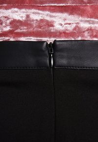 Svart dragkedjeskirt med midja i konstläder, med en slät textur. Bakgrunden är en rosa plyschtyg.