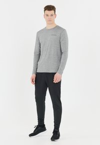 Ljust grå långärmad tröja med "ENDURANCE" logotyp, kombinerad med figurnära svarta byxor med fickor och svarta sportskor.