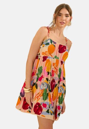 Naine kannab varrukateta põlvpikkust kleiti, millel on värvikad puu- ja lehemustrid, kaunistatud kuldsete rõngaste ja käevõrudega.