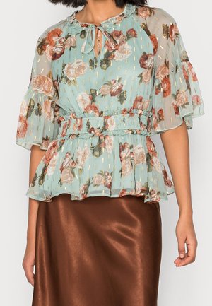 Jasnoniebieska kwiecista bluzka ze złotymi akcentami, falbaniaste rękawy, wiązanie przy dekolcie oraz taliowany pas, zestawiona z błyszczącą brązową satynową spódnicą.