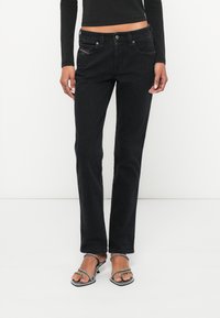 Čierne džínsy z denimu s rovnými nohavicami, piatimi vreckami a kontrastným šitím. Nosia sa s sandálmi na vysokom podpätku so remienkami.