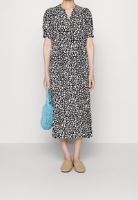 Schwarz-weißes Leopardenmuster-Kleid mit kurzen Ärmeln und Knopfverschluss; kombiniert mit einer strukturierten blauen Tasche und beigen Slippern.